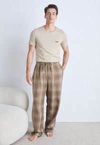 Beige t-shirt with small black logo on chest, paired with brown plaid lounge pants featuring an elastic waistband and drawstring.
