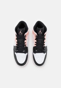 Para czarnych, białych i jasnoróżowych sneakersów Air Jordan widziana z góry, ukazująca czarne sznurowadła i logo Jumpman na językach.