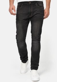 Zwarte denim jeans met een slim fit ontwerp, voorzien van contrasterende stiksels en een vijf-vakken indeling, gecombineerd met witte sneakers.