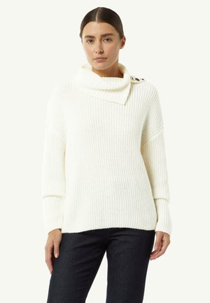 White knitted sweater with a cowl neck, ribbed texture, and three buttons on the left shoulder. Worn with dark jeans.