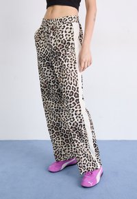 Leopard print trousers with elastic waistband, side white stripes, and a loose fit. Paired with bright pink sneakers. Soft fabric texture.