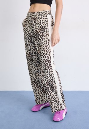 Leopard print trousers with elastic waistband, side white stripes, and a loose fit. Paired with bright pink sneakers. Soft fabric texture.
