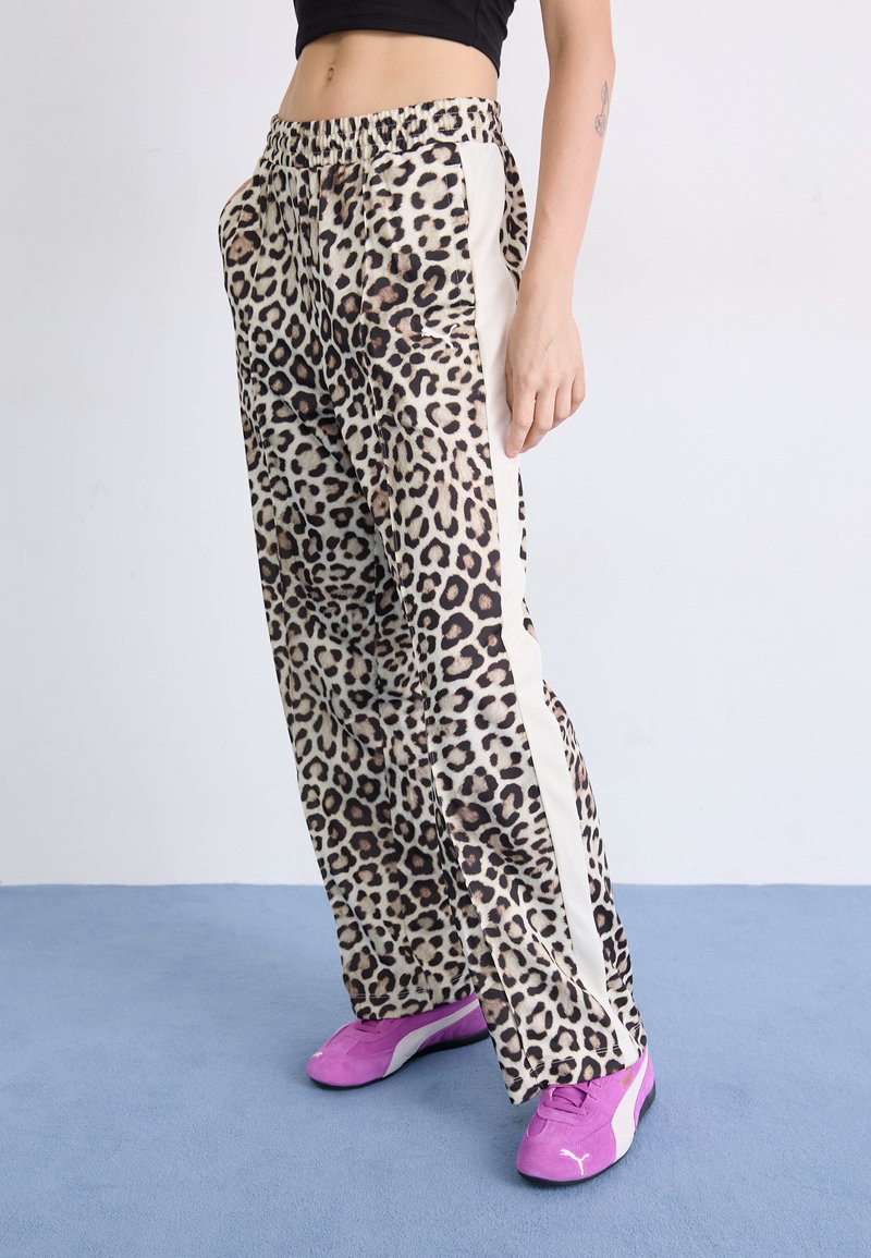 Leopard print trousers with elastic waistband, side white stripes, and a loose fit. Paired with bright pink sneakers. Soft fabric texture.