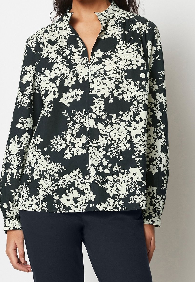 Chemise noire avec un motif floral blanc, col à revers et manches longues. Confectionnée dans un tissu léger, elle offre une coupe décontractée.