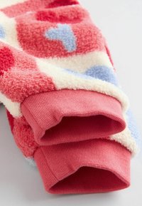 Housut fleece-kankaasta, joissa on vaaleanpunaisia, punaisia ja sinisiä pilkkuja; pehmeä rakenne; ribatusta vaaleanpunaisesta resorista; kerma tausta; kuviollinen malli.