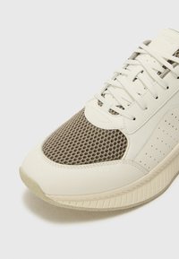 Leichte Sneakers mit einer weißen Lederbasis und einem grauen Mesh-Obermaterial, durchbrochenenDetails und einer strukturierten, gemusterten Sohle.