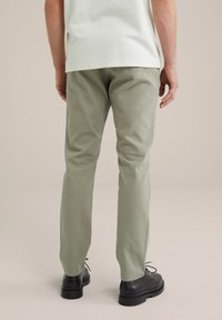 Pantaloni twill verzi cu o croială slim, featuring buzunare laterale, purtați cu pantofi negri cu șireturi. Partea de sus este un tricou de culoare deschisă.
