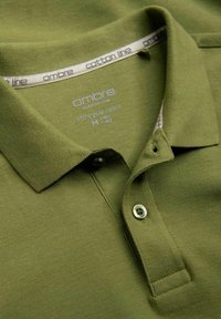 Olive vihreä polo-paita, joka on valmistettu 100% puuvillasta. Paita sisältää teksturoidun kankaan, taitettavan kauluksen ja kaksi nappia napituslistassa.