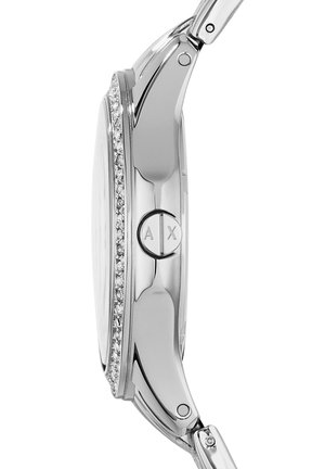 Silverfärgad armbandsur med rund klockkapsel, kristallaccenter, polerad yta och en logotyp på sidan. Justerbart metallarmband.