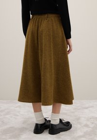 Jupe marron texturée en ligne A avec une taille élastique. Portée avec des chaussettes blanches côtelées et des chaussures noires à lacets.