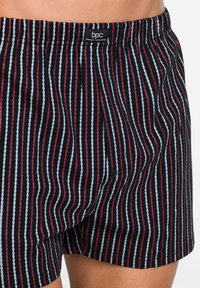 Boxer neri con strisce verticali di diversi colori: rosso, blu e bianco, dotati di un elastico in vita e un bottone frontale.