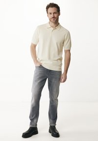 Kortärmad, ljusgul polo med stickad struktur; kombinerad med ljusgrå jeans och svarta ankelstövlar. Enkel, avslappnad outfit.