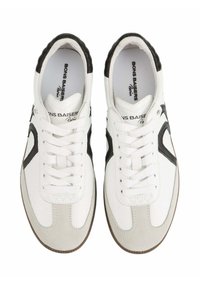 Baskets blanches avec accents noirs, tige en cuir, semelle en caoutchouc, lacets plats et logo sur la languette. Suède texturé dans la zone des orteils.