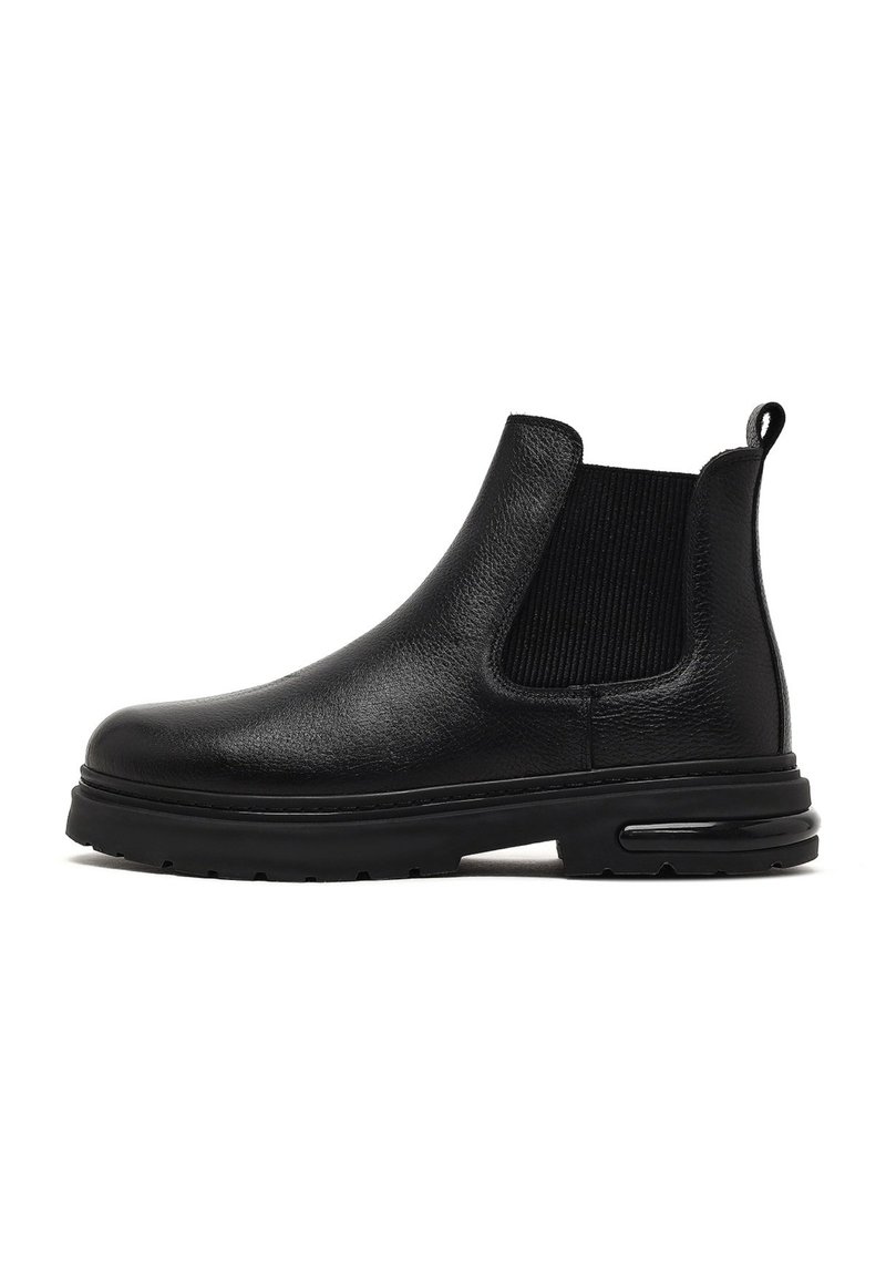 Botines Chelsea negros hechos de cuero texturizado, con paneles laterales elásticos, una pestaña para facilitar el calzado y una suela de goma gruesa con amortiguación de aire.