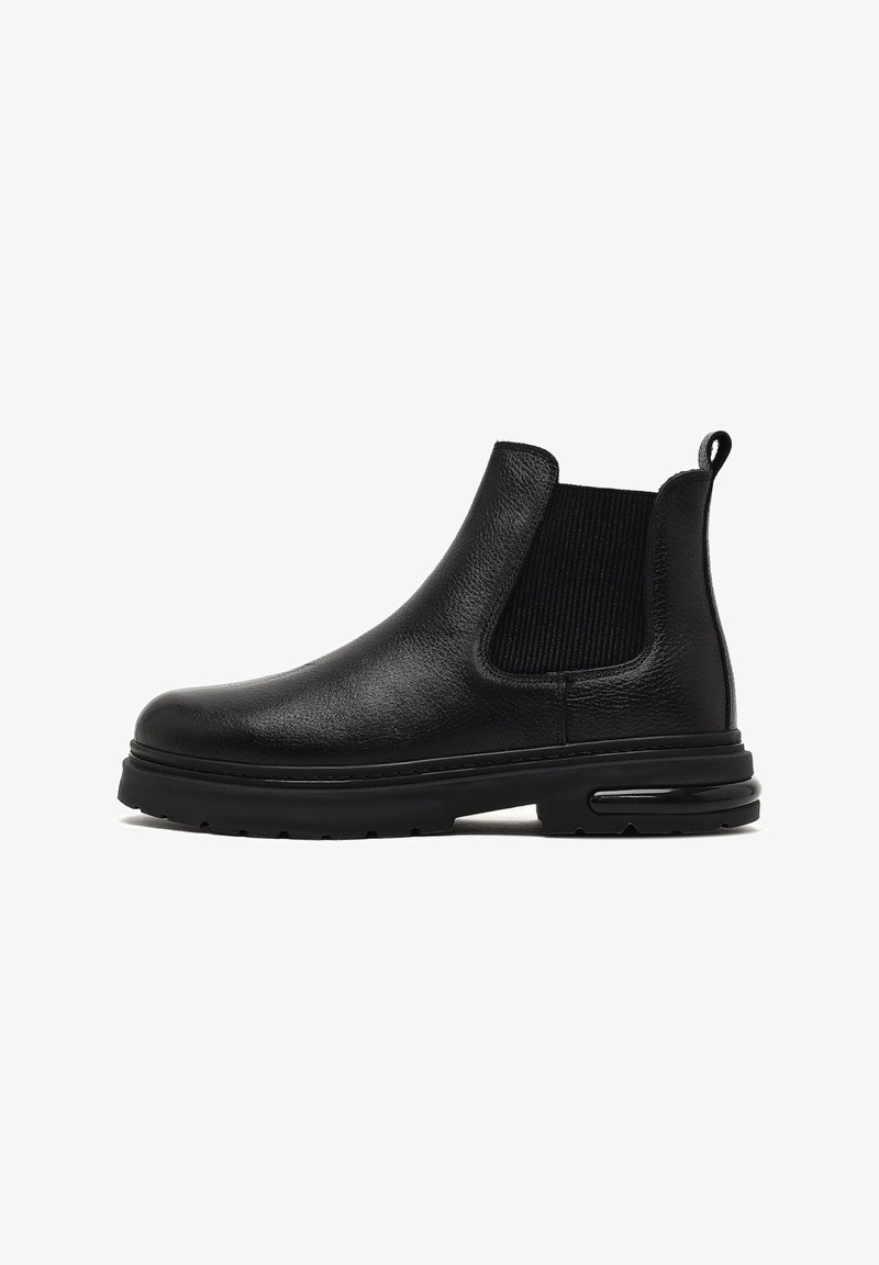 Botines Chelsea negros hechos de cuero texturizado, con paneles laterales elásticos, una pestaña para facilitar el calzado y una suela de goma gruesa con amortiguación de aire.