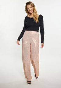 Schwarzes geripptes Langarmoberteil, kombiniert mit hochtaillierten, weit geschnittenen, rosa Pailletten-Hosen mit glatter Textur und metallischem Glanz.