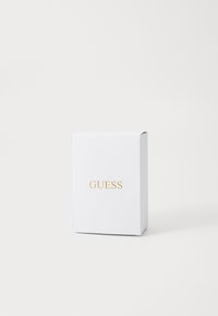 Cutie albă dreptunghiulară cu suprafață texturată �și logo-ul aurit "GUESS" centrat în față, pe un fundal alb simplu.
