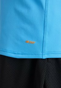 Blauw sportshirt met oranje "B DRY"-logo boven zwarte mesh korte broek, met nadruk op vochtregulerende stof en stikseldetails.