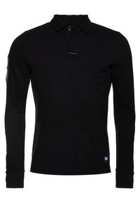 Polo noir à manches longues avec col boutonné, en tissu texturé, et une petite patch logo à l'ourlet. Présente des poignets côtelés.