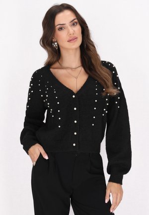 Schwarze kürzere Strickjacke mit V-Ausschnitt, verziert mit weißen Perlen auf den Schultern und der Vorderseite. Hergestellt aus einem weichen, strukturierten Stoff.
