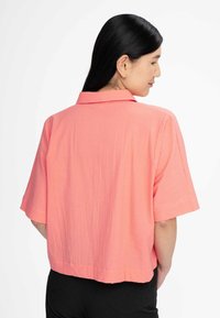 Korte mouw, gekraagde shirt van textuurlijke koraalstof, met een boxy fit en een rechte zoom, zichtbare naadstiksels aan de achterkant.