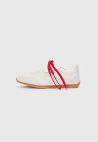 White athletic shoe with woven texture, rubber sole, and red laces. Features padded collar and minimalistic design elements.