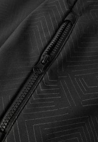 Tissu noir avec un motif géométrique et un gros plan d'une fermeture éclair noire partiellement ouverte traversant le cadre en diagonale.