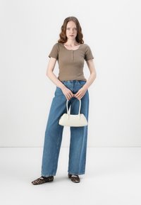 Haut côtelé marron à manches courtes, jeans large taille haute en denim bleu clair, chaussures léopard noir et marron, et un petit sac à main blanc.