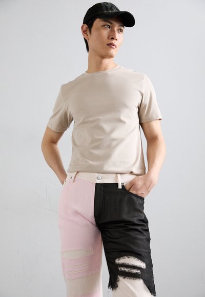 T-shirt aderente beige abbinato a jeans in patchwork, con sezioni rosa e nere, dettagli strappati e accessori metallici in vita.