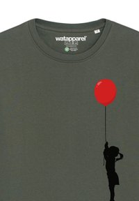 Donkergroen katoenen t-shirt met een zwarte silhouet van een kind dat een rode ballon vasthoudt, gedrukt op de voorkant. Ronde hals en korte mouwen.