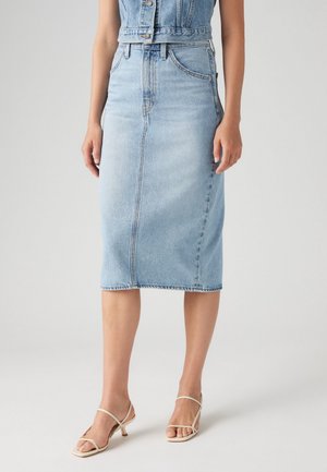 Kvinde iført et lyseblåt denim blyantskjørt kombineret med en matchende ærmeløs denimtop og beige remsandaletter med hæl.