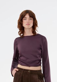 Purple satin long-sleeve top with a square neckline and a cropped silhouette. Smooth texture with a relaxed fit, paired with brown corduroy pants.