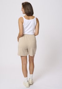 Shorts en coton beiges avec une ceinture élastique, des poches latérales et une poche arrière, associés à un haut sans manches blanc et des chaussettes blanches.
