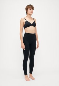Schwarzer Bralette mit dünnen Trägern und einem tief ausgeschnittenen Design, kombiniert mit hochgeschnittenen schwarzen Leggings. Beide bestehen aus dehnbarem Stoff.