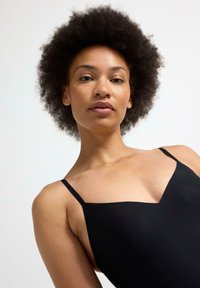 Costume da bagno senza maniche di colore nero con scollatura a V, dotato di spalline sottili e una texture liscia, indossato da una persona su uno sfondo chiaro.
