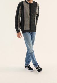 Maglione a maglia grigio e nero, con maniche lunghe, abbinato a jeans azzurri chiari e sneakers nere con strisce bianche.