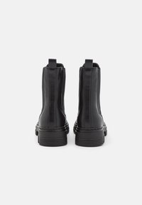 Mustat nahkaiset nilkkurit, joissa on sileä pinta, joustavat sivupaneelit ja vetokahvat. Paksu kumipohja, jossa vaakasuorat urat pitoon.