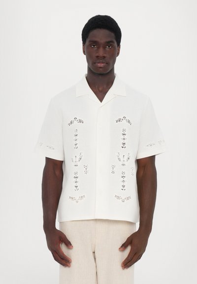 White short-sleeve shirt with openwork details, a button-up front, and a revere collar. Fabric has a light texture suitable for warm weather.