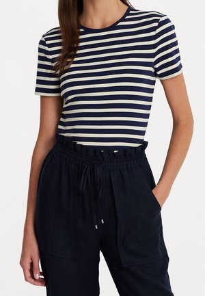 Gestreept T-shirt in marineblauw en roomkleur, met korte mouwen en ronde hals, gecombineerd met donkere, losvallende broek met elastische tailleband en zakken.