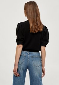Suéter negro texturizado con mangas abullonadas, combinado con jeans de tiro alto en azul claro que presentan bolsillos traseros y un acabado desgastado.