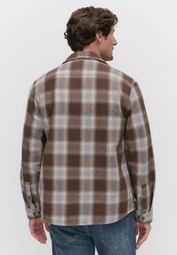 Brown and gray plaid shirt featuring a buttoned collar, long sleeves, and a curved hem. Made from a textured, warm fabric.