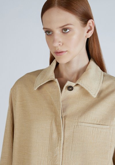 Giacca in corduroy beige con colletto a punta, bottoni frontali e tasca sul petto; presenta una trama a coste verticali e una vestibilità rilassata.