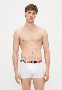 Baltas bokseršorti ar melnu vidukļa lentu, uz kuras ir sarkans "DIESEL" logotips, gluda auduma, vidēja augstuma dizains un pieguloša forma.