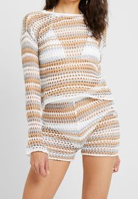 Ensemble haut et short en tricot crocheté en blanc, beige et argenté. Caractérisé par une maille ajourée, des manches longues et une coupe décontractée.