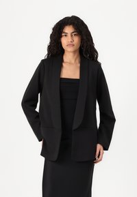 Černý blazer s širokými klopami a dlouhými rukávy, který má uvolněný střih a dvě přední kapsy. Hladká tkanina a strukturovaný design.