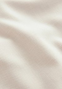 Tissu beige clair avec un motif de tissage texturé, doté d'une surface lisse et douce qui semble légèrement froissée.