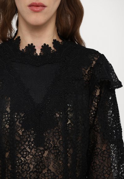 Black lace top features floral patterns, a high neck with scalloped edges, and textured layers. Semi-sheer material adds depth.