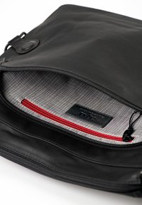 Zwarte leren tas met een ritssluiting, voorzien van een grijze voering met patroon en een rood binnenvak met ritssluiting. Logo-label zichtbaar aan de binnenkant.