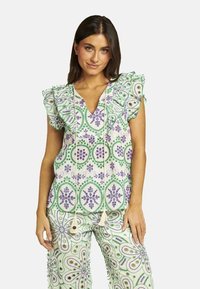 Top blanco con patrones florales en verde y morado, mangas con volantes y escote en V; combinado con pantalones a juego con el mismo patrón y borlas.