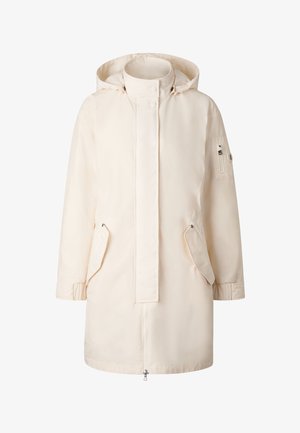 Lang, cremegul parka med hætte, forlynlås dækket af klap med trykknapper, to skrå lommer og lynlåslomme på venstre ærme.